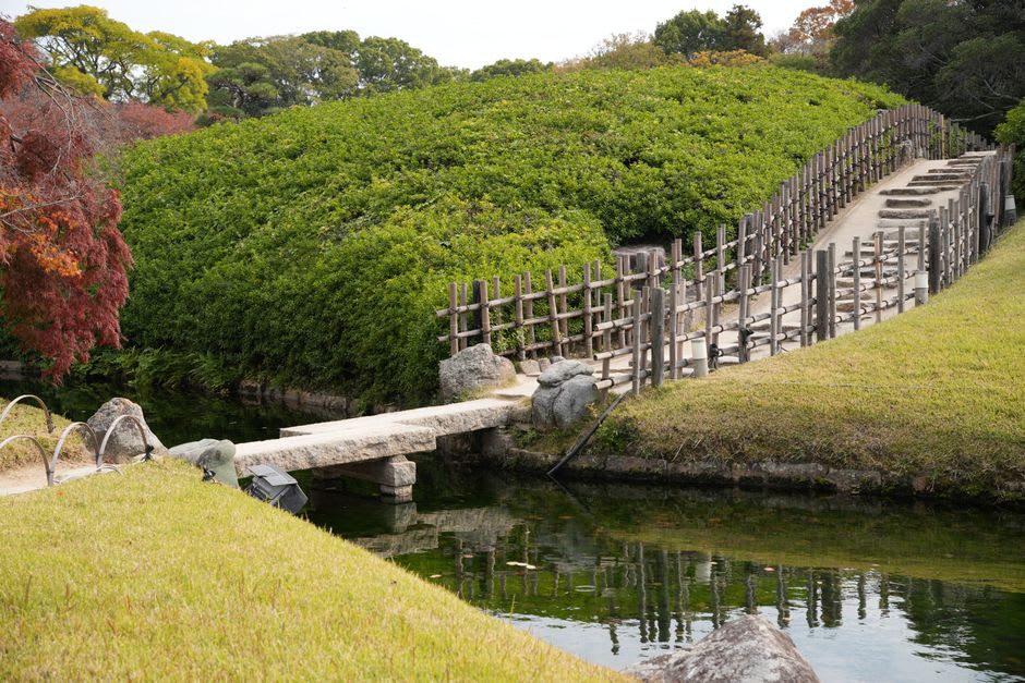 The black-walled Okayama Castle with gold trim reflected in the river at dusk, an arched bridge leading toward it