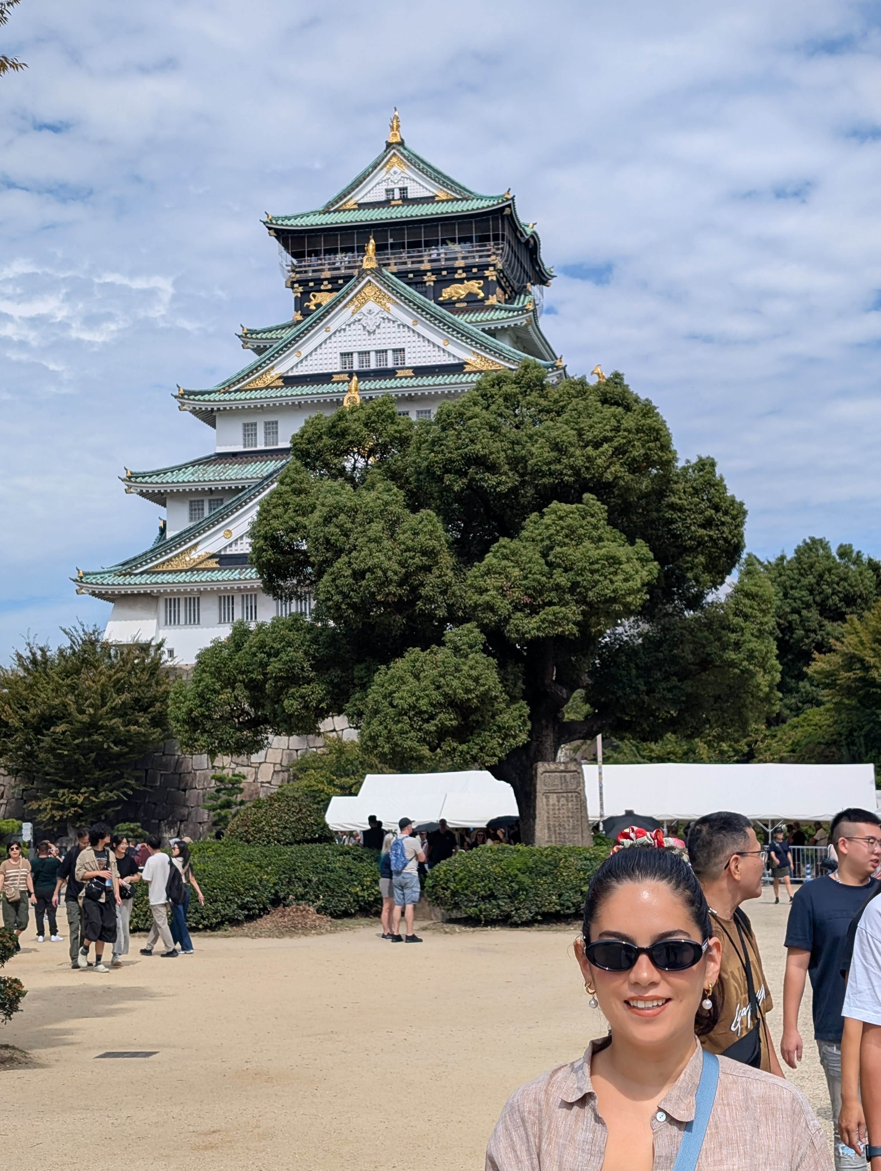 Lia in front of Osaka Castle — sunglasses on, the white-and-gold tower rising above the trees behind her