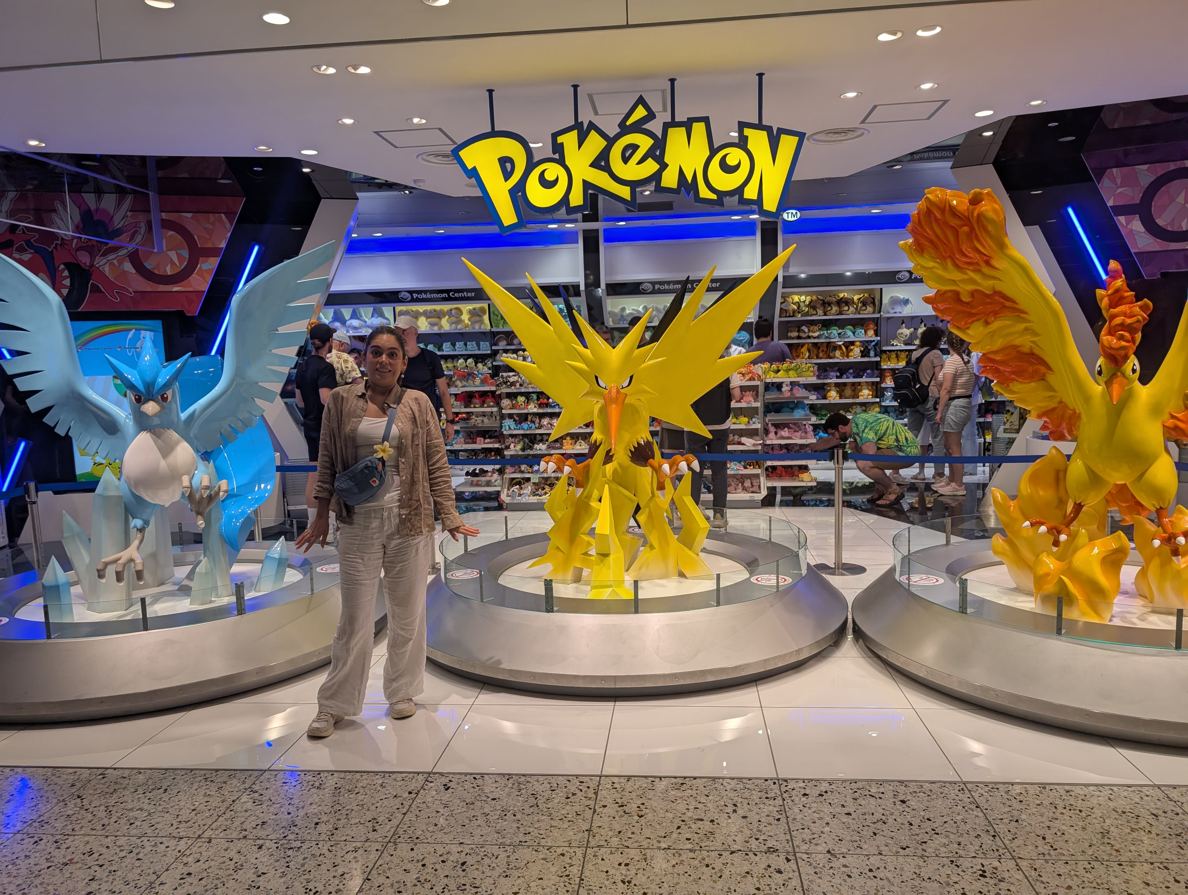 Lia at the Pokémon Center in Namba — standing between life-sized Articuno, Zapdos, and Moltres statues, trying to maintain composure