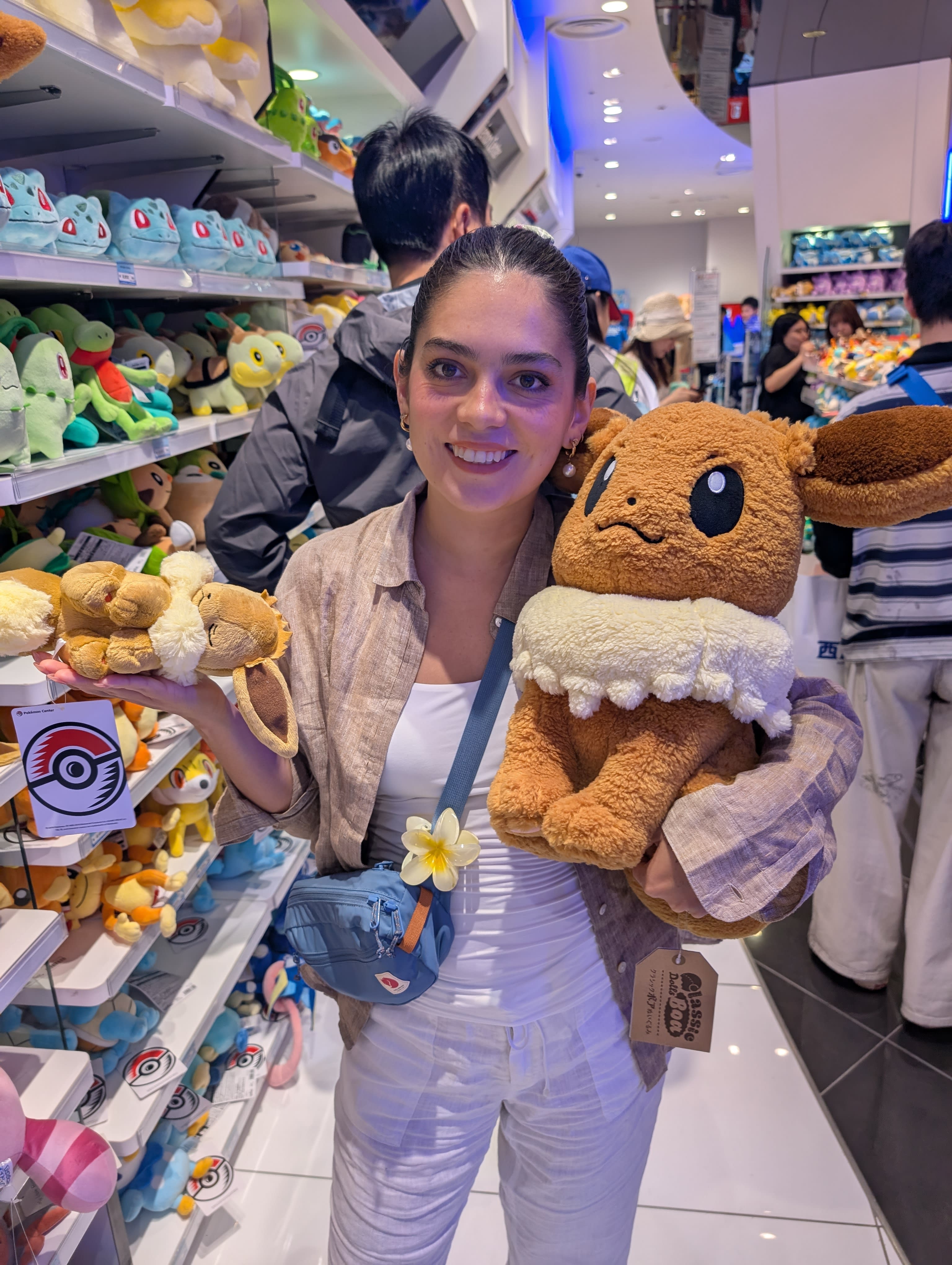 Lia holding an enormous Eevee plush at the Pokémon Center — her grin communicating that this purchase is not up for discussion