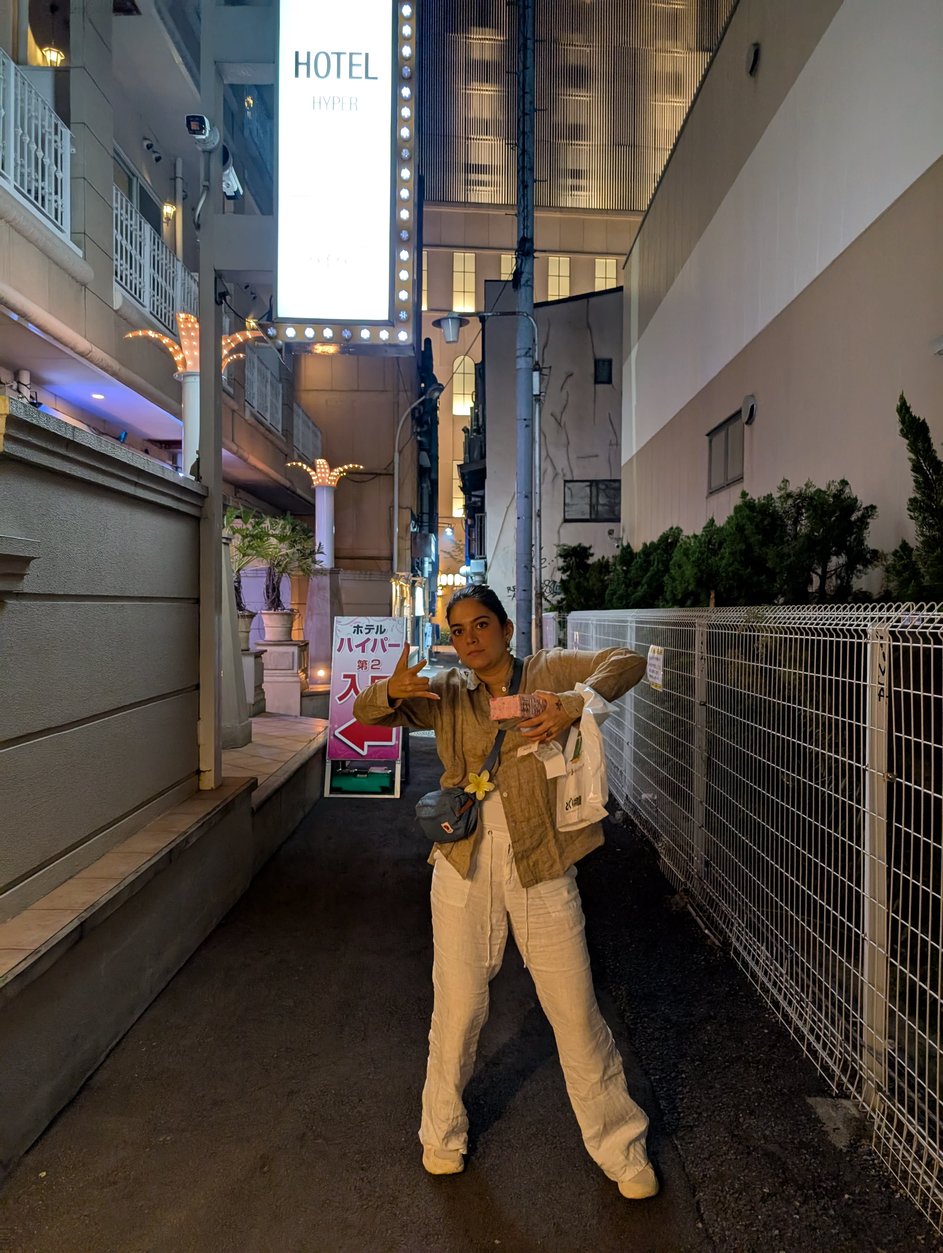 Lia in a Namba back alley at night — hotel signs above, the warm glow of the city behind her, striking a pose that says Osaka has been thoroughly conquered