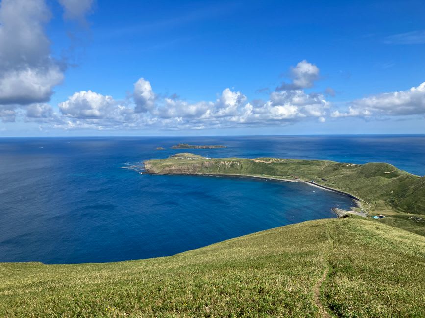 A cliff-top coastal trail on Rebun's wild western side, green meadow above sheer drops to the crashing Sea of Japan