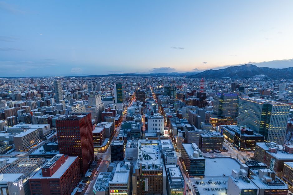 Snow-dusted mountains rising at the edge of Sapporo, ski runs threading down the slopes above the city's low northern rooftops