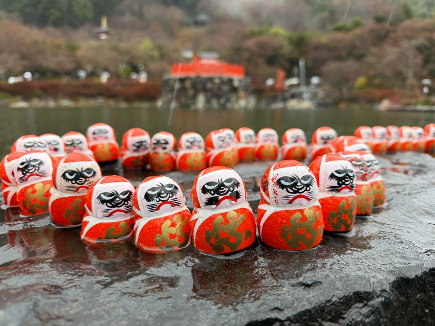 Weathered hands painting the eyebrow of a red daruma doll in a Takasaki workshop