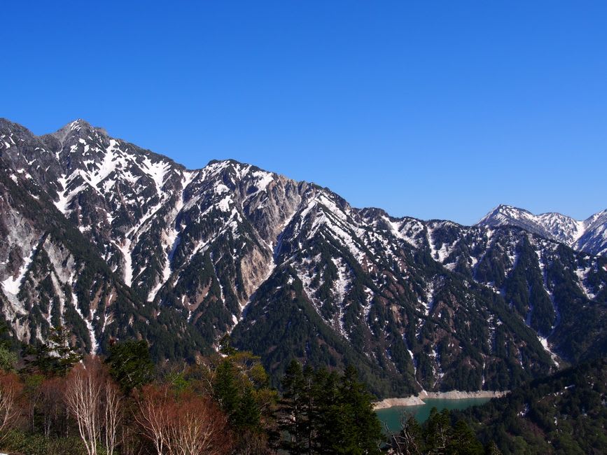 The great curved wall of the Kurobe Dam holding back an emerald reservoir, a plume of released water thundering down into the gorge below