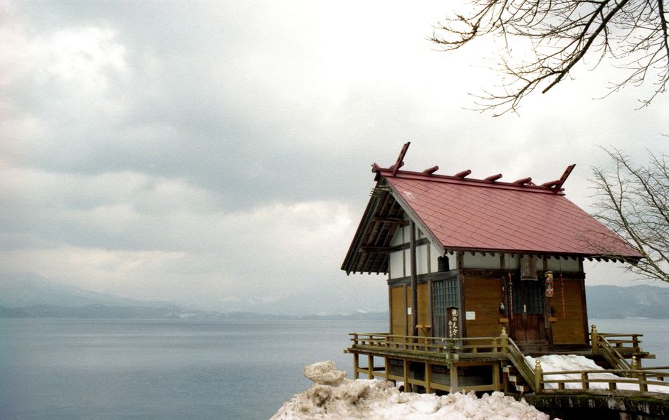 A milky-white open-air hot-spring bath at Nyūtō Onsen surrounded by thatched wooden buildings and dense green forest