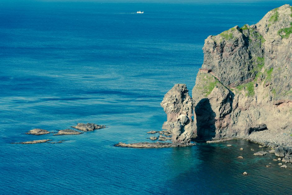 Visitors sitting on the flat cliff-top ledges above crashing surf at Tojinbo