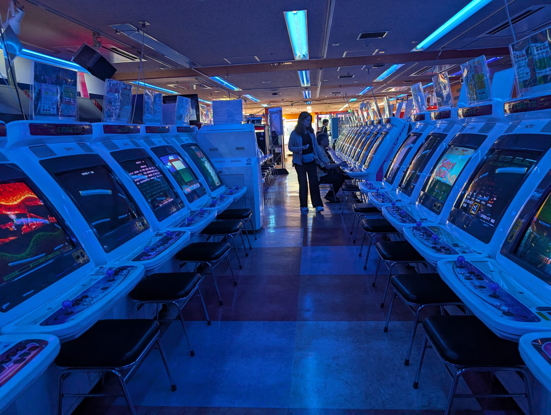 Rows of blue-lit arcade cabinets stretching into the distance at an Akihabara game centre