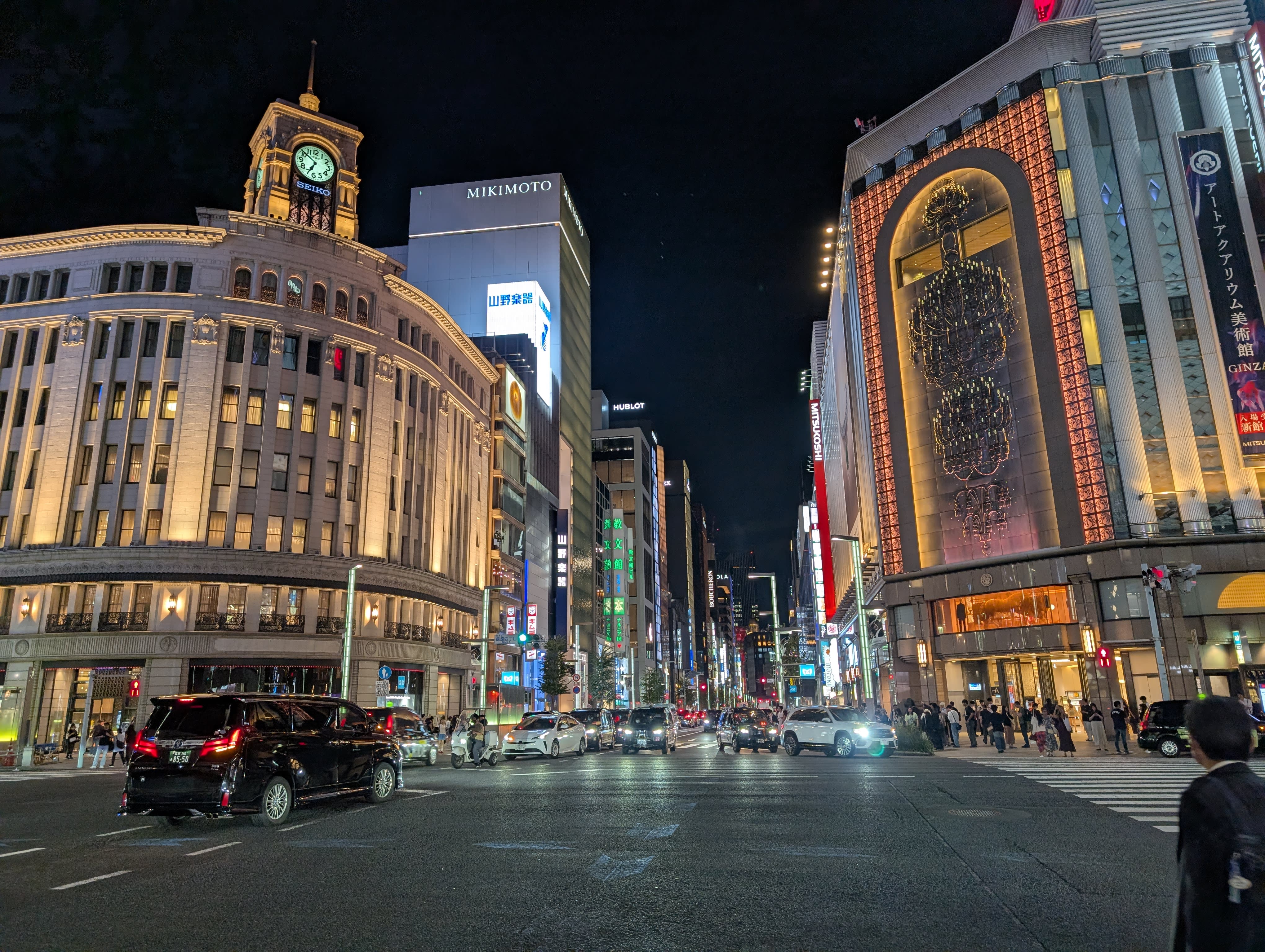 Ginza at night — the illuminated Wako clock tower, Mikimoto building, wide avenues gleaming, traffic and pedestrians below