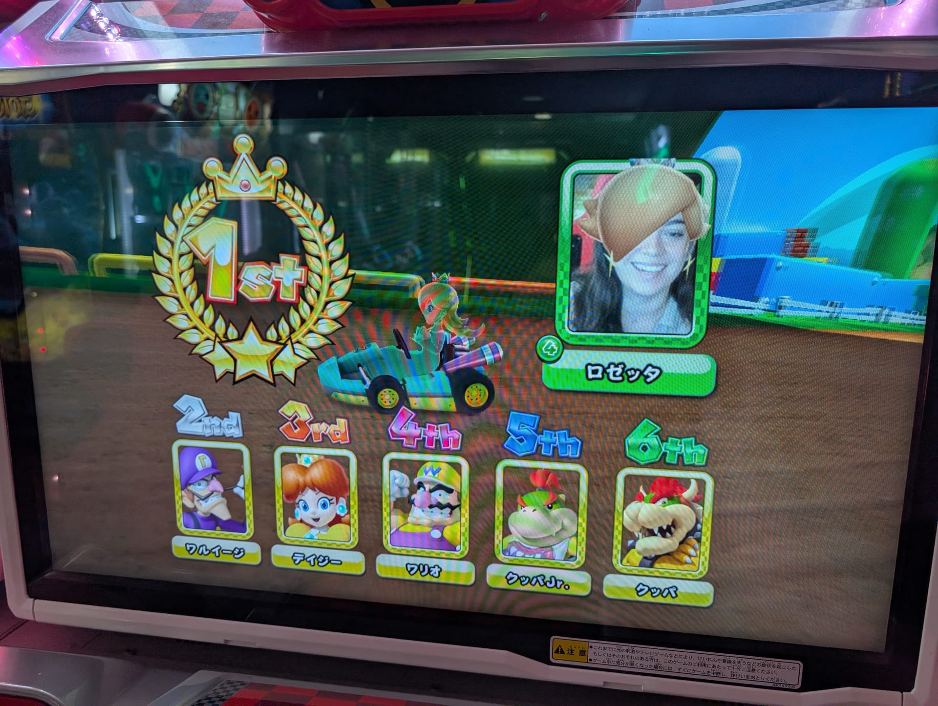 Lia's Mario Kart victory screen showing 1st place — her face captured by the cabinet's camera, looking triumphant
