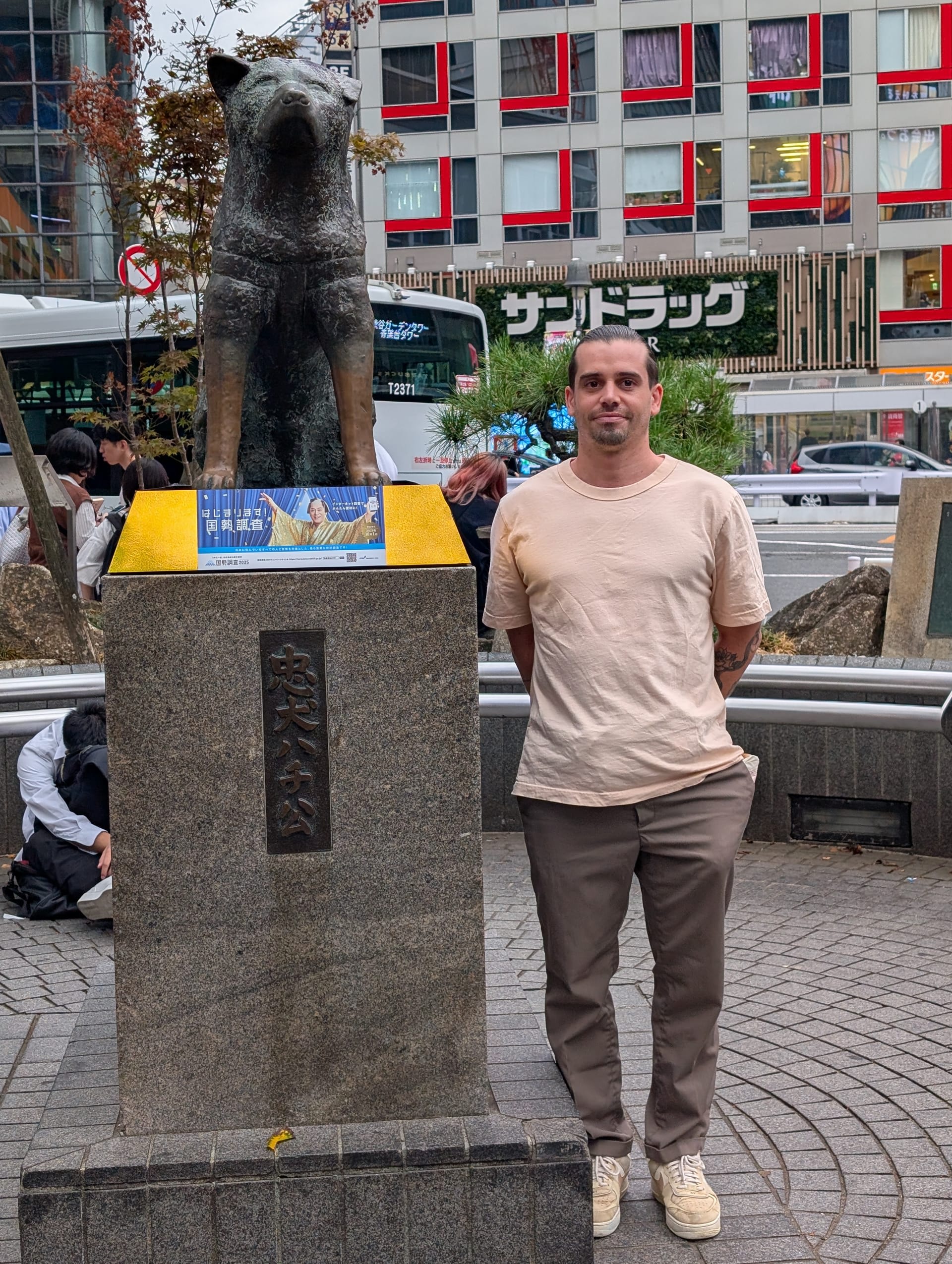 Pierre standing next to the Hachiko statue outside Shibuya Station — the bronze dog on his pedestal, the city rushing behind