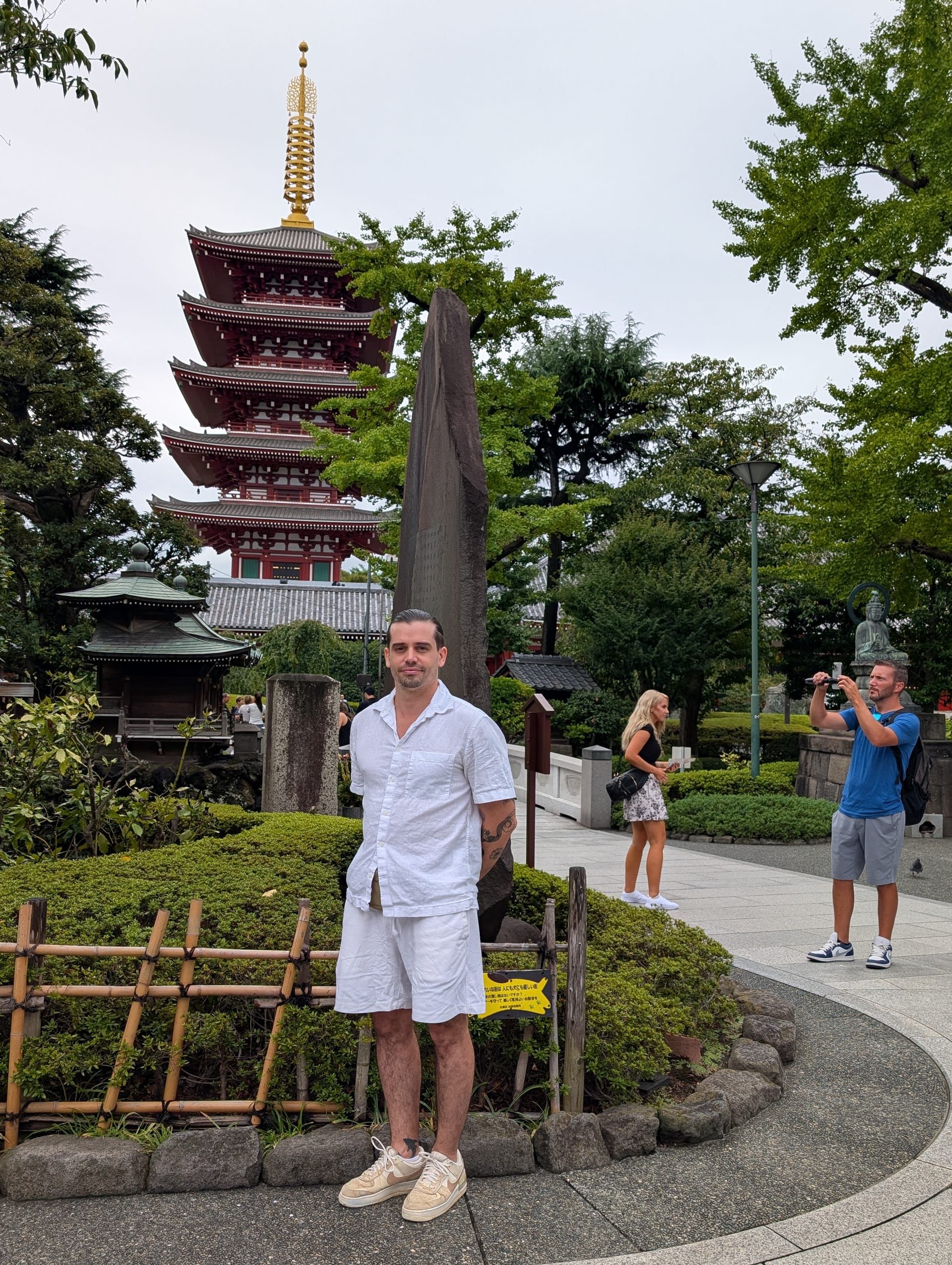 Pierre in front of the five-story pagoda at Senso-ji, wearing white, tourists and greenery behind him