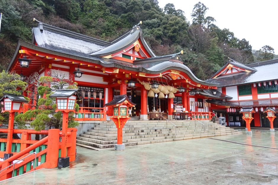A tunnel of vermilion torii gates climbing the wooded hillside to Taikodani Inari shrine above Tsuwano, sunlight cutting between the red pillars