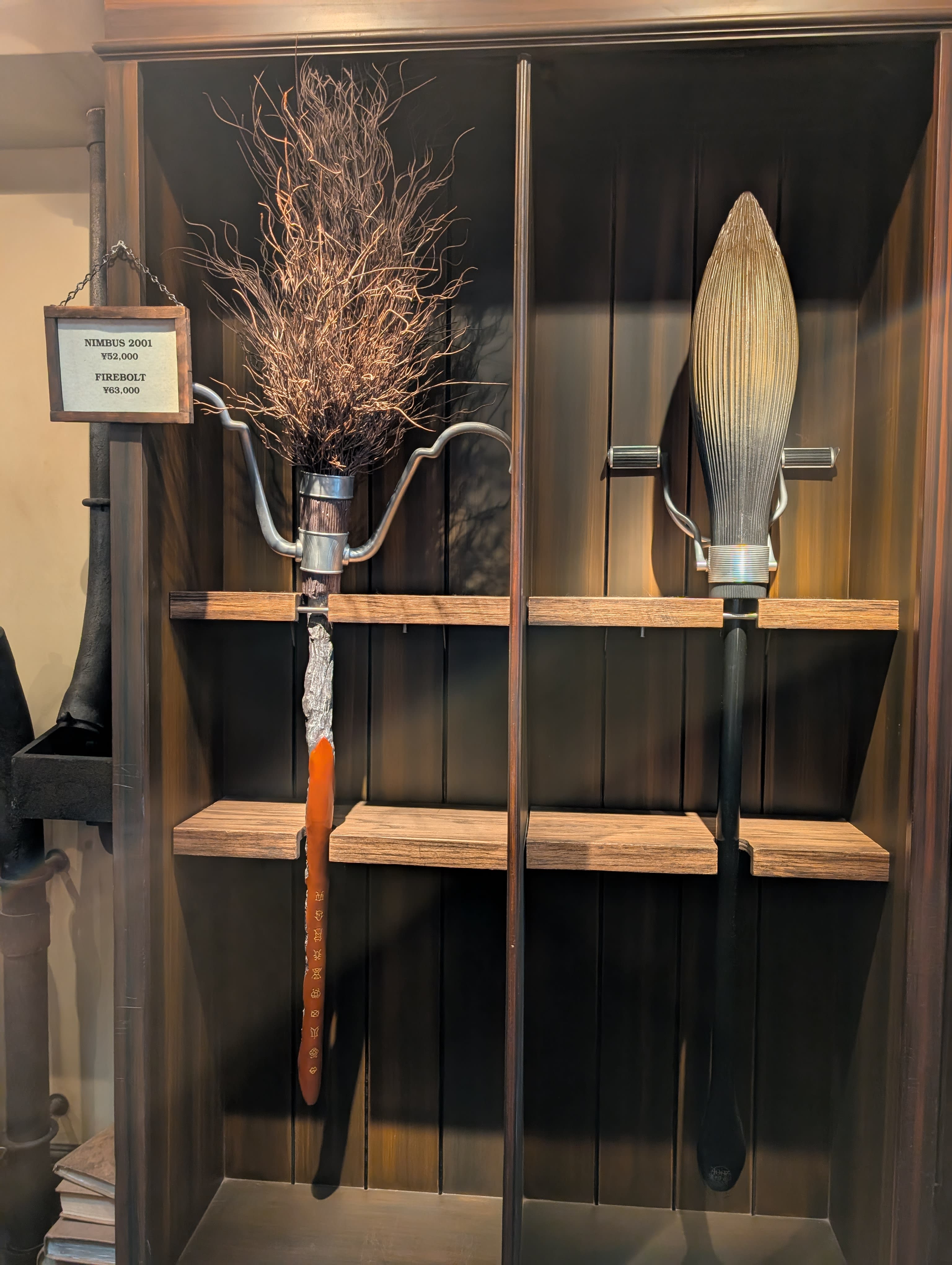Quidditch broomsticks on display — the Nimbus 2000 and Firebolt mounted on a dark wooden wall, looking ready to be grabbed