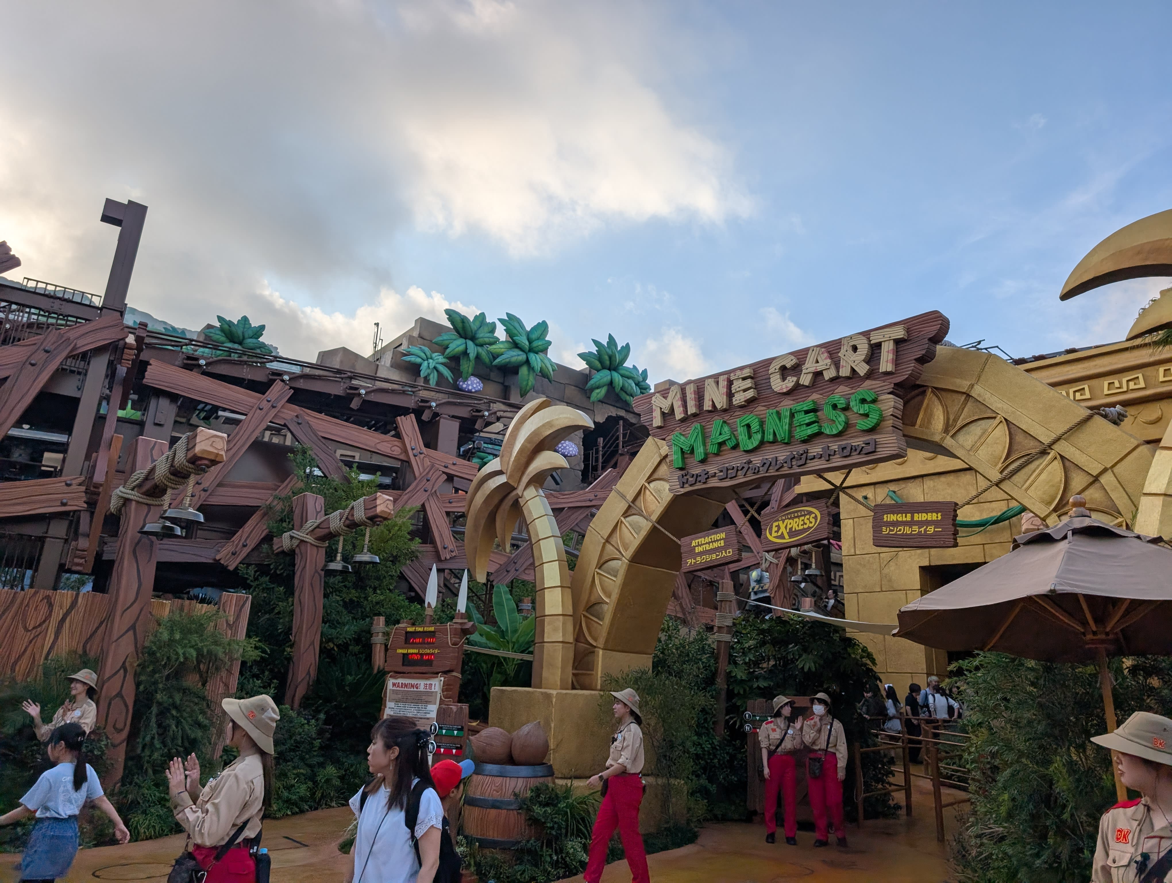 The entrance to Mine Cart Madness in Donkey Kong Country — the banana archway, the jungle theming, staff in explorer gear, barrels and palm trees everywhere