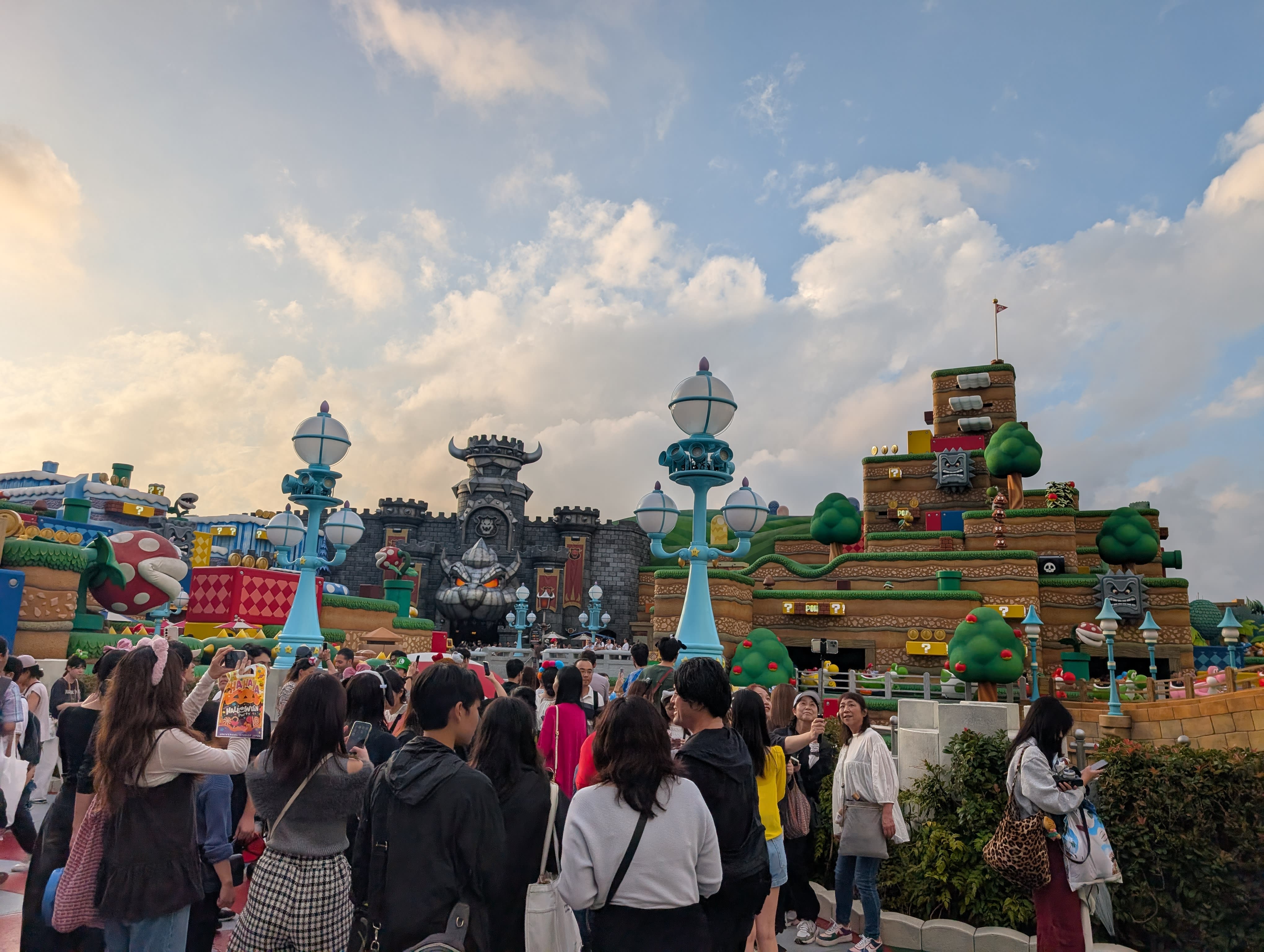 Super Nintendo World at golden hour — the full panorama of the Mushroom Kingdom, crowds below, Bowser's Castle and the question blocks catching the late light
