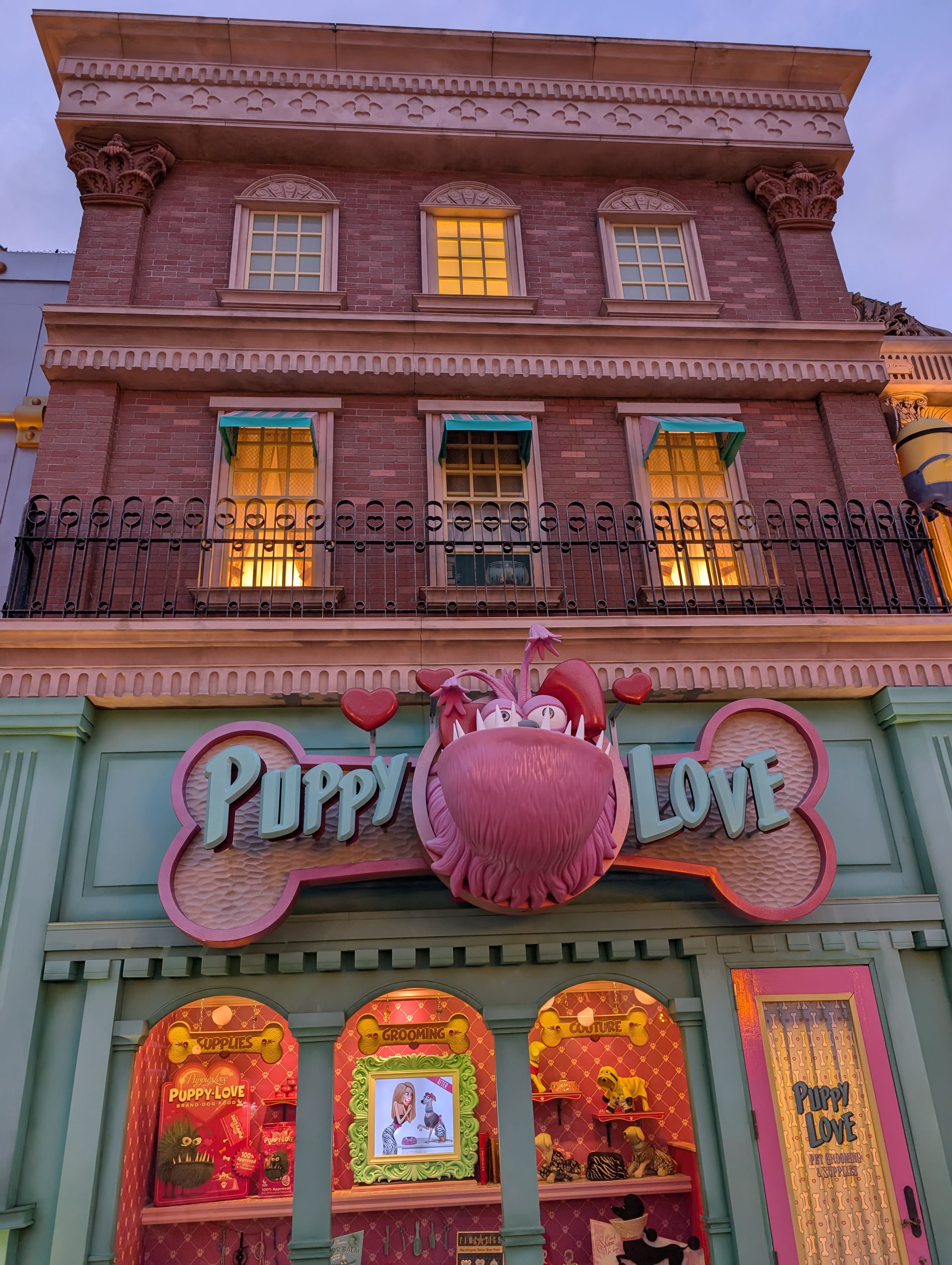 The Puppy Love shop — a giant pink creature above the entrance, the pastel facade glowing at dusk, hearts and bones in the signage