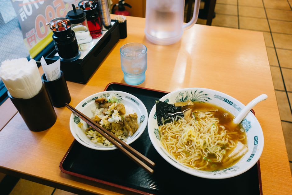 A steaming bowl of Wakayama-style tonkotsu-shoyu ramen on a wooden counter with pressed mackerel sushi