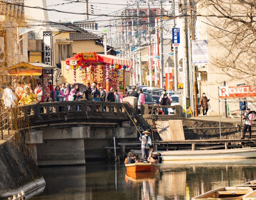 A low donkobune punt gliding beneath a small stone bridge on a willow-lined Yanagawa canal
