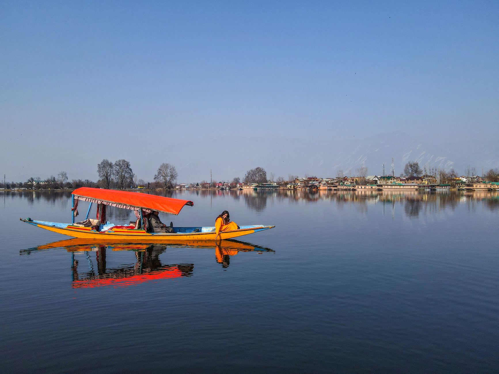 Nagin Lake in early morning, mirror-still water reflecting the surrounding willows and pine-covered hills, a single shikara visible in the distance