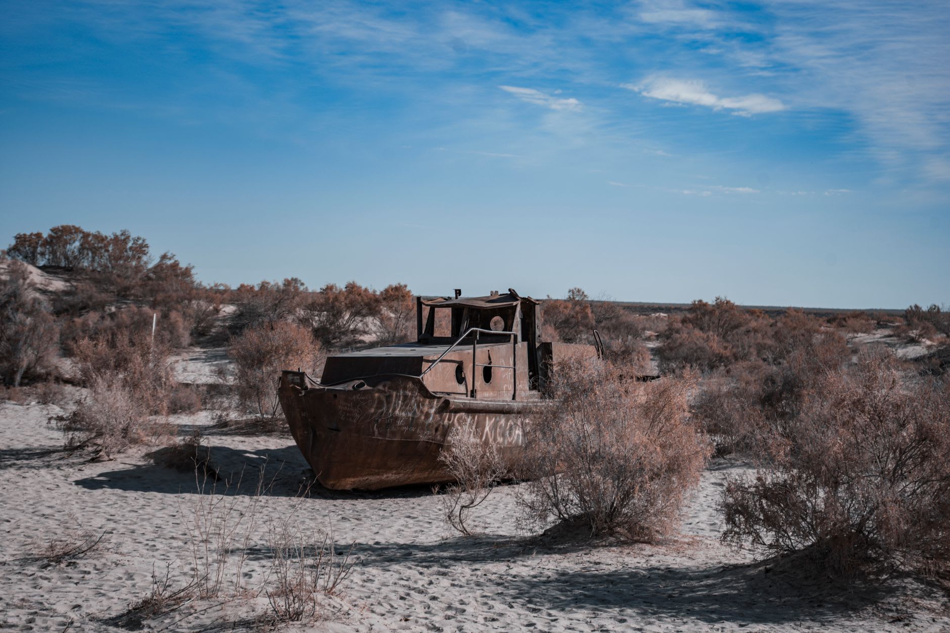 A wide view of the salt flat surrounding the rusting ship hulls, white salt crust stretching to the flat horizon under a vast Kazakhstan sky