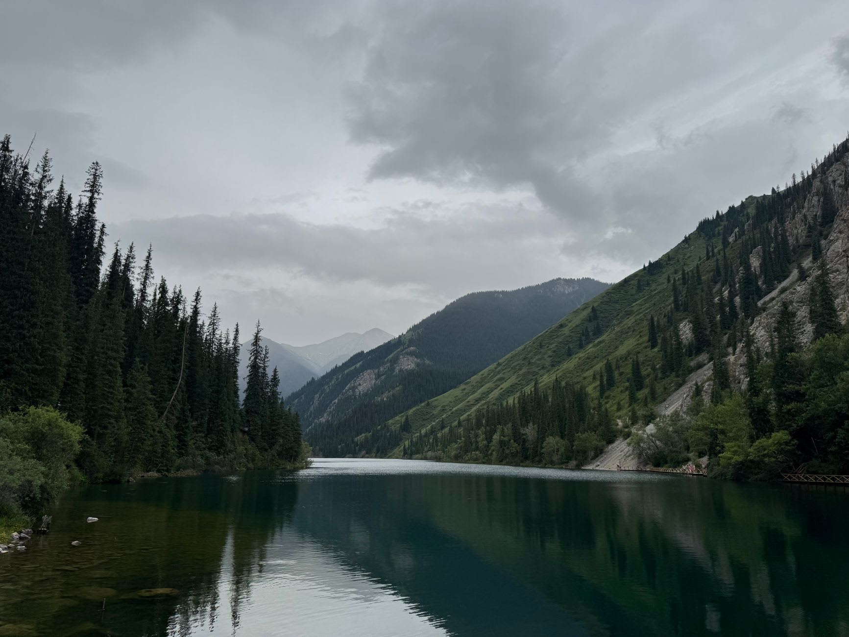 The lower Kolsai Lake with its wooden jetty and turquoise waters, surrounded by pines ascending to the snowline
