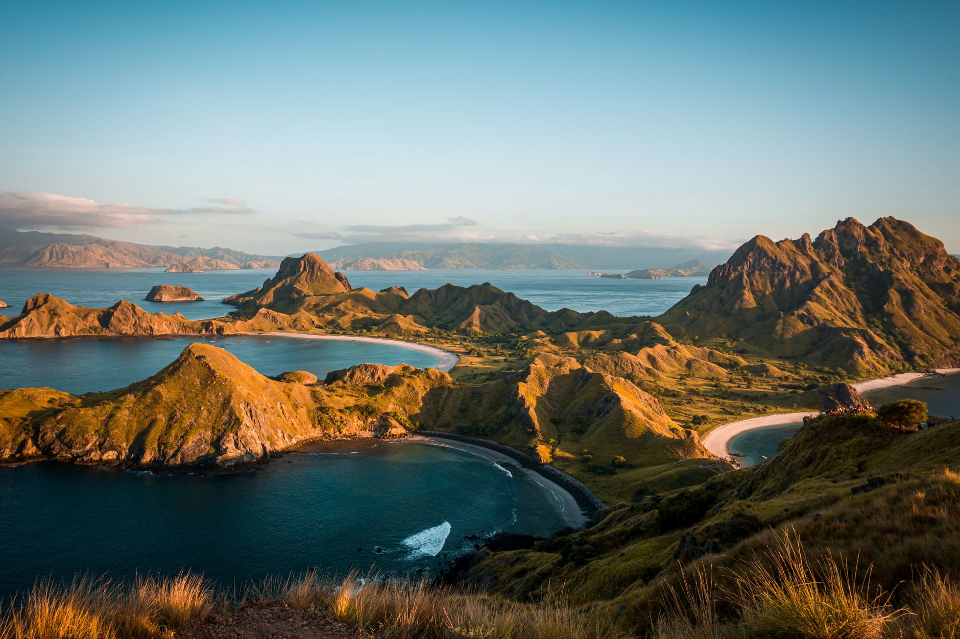 View from a Rinca Island ridgeline looking across the strait toward Komodo Island, golden savanna and turquoise water below