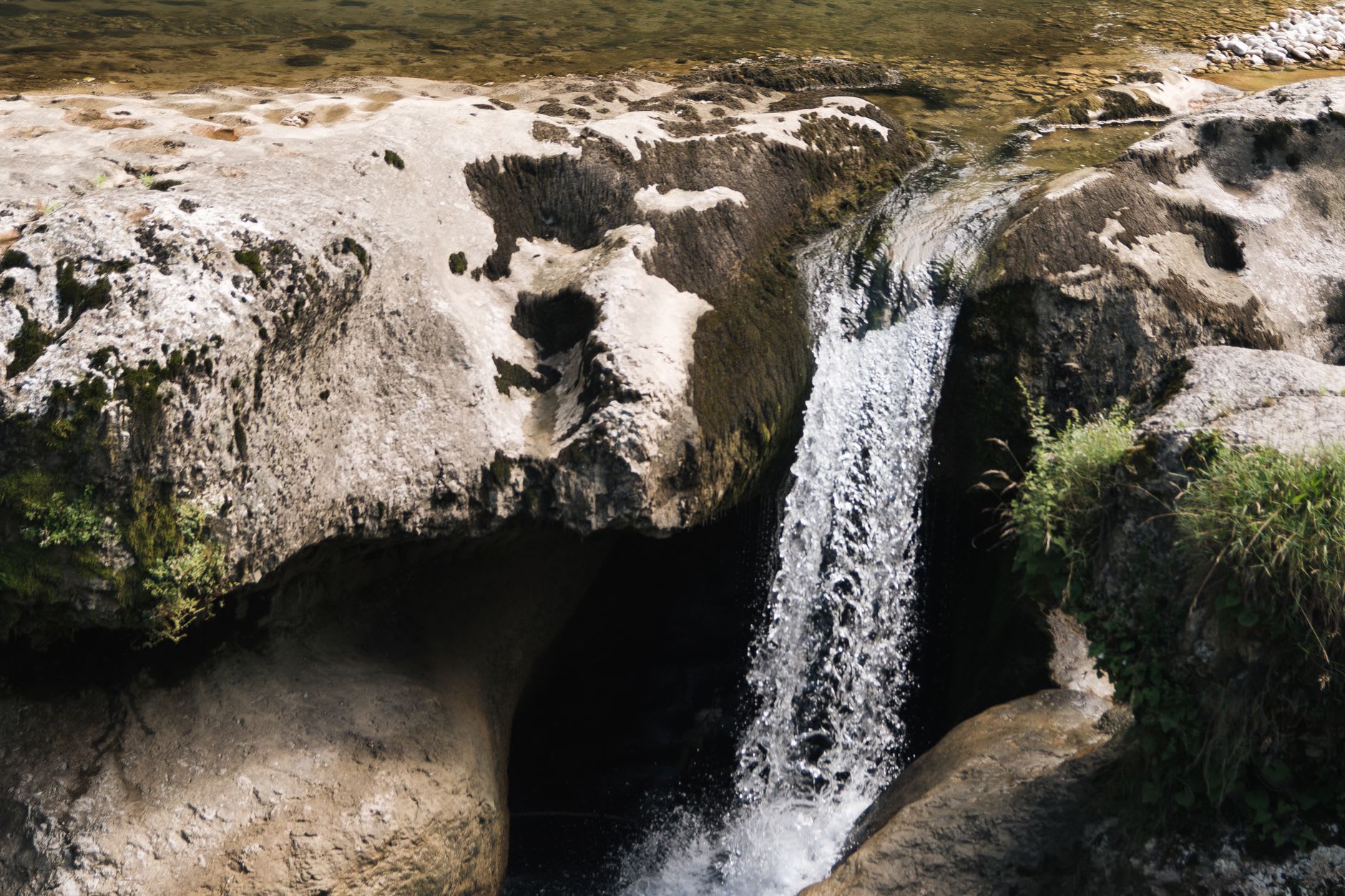 Un randonneur debout au bord d'une vasque de cascade de Mirusha, l'eau émeraude remplissant le cadre en dessous