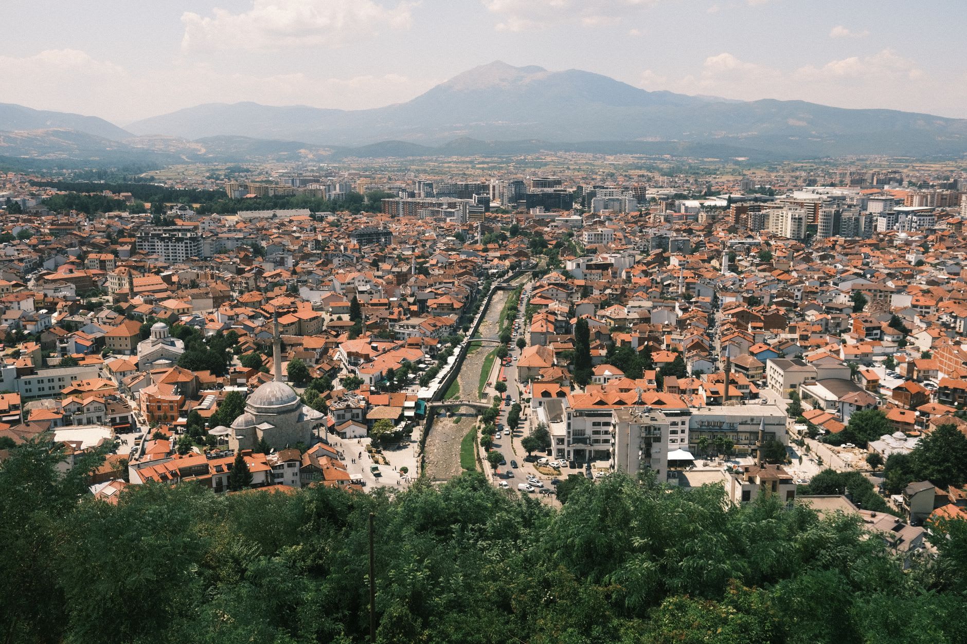 La rivière Ibar traversant le centre de Mitrovica, les terrasses de cafés et le boulevard piétonnier de Mitrovica Sud visibles sur la rive droite