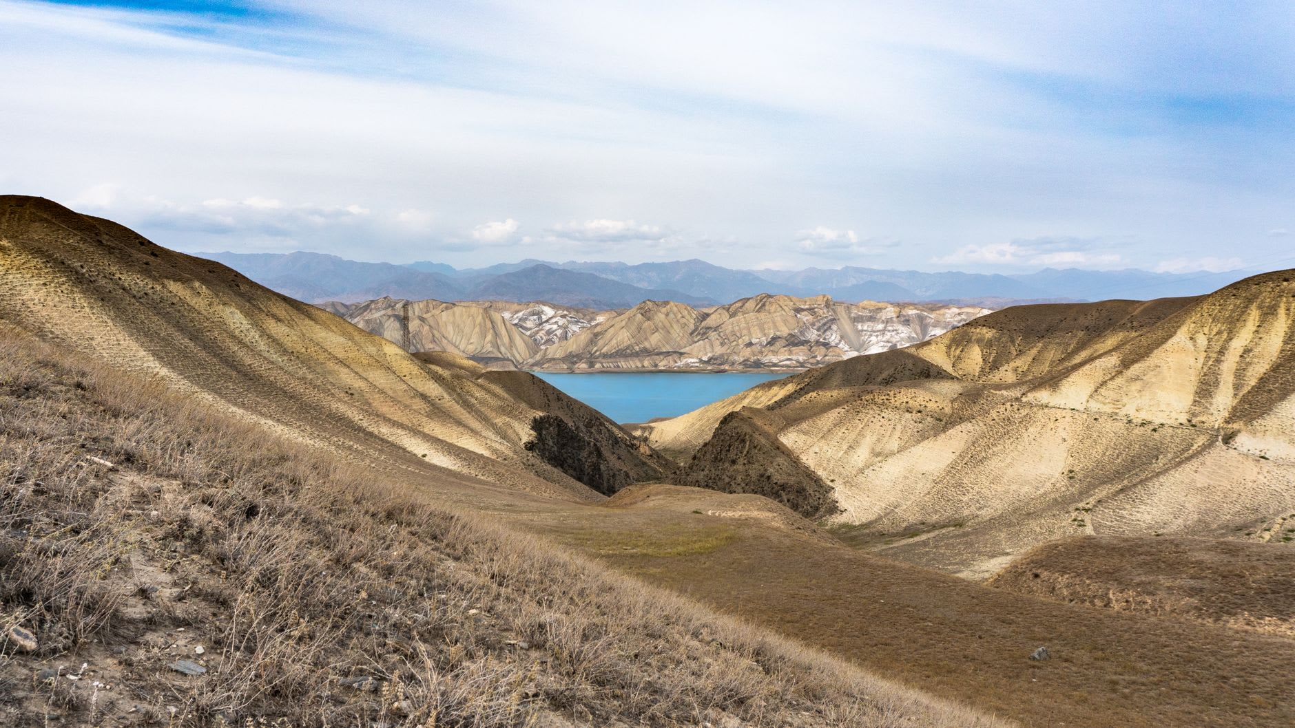 The broad meadows of the Altyn-Arashan valley with the Arashan river winding through, wooden guesthouses in the foreground and snow-capped peaks rising behind