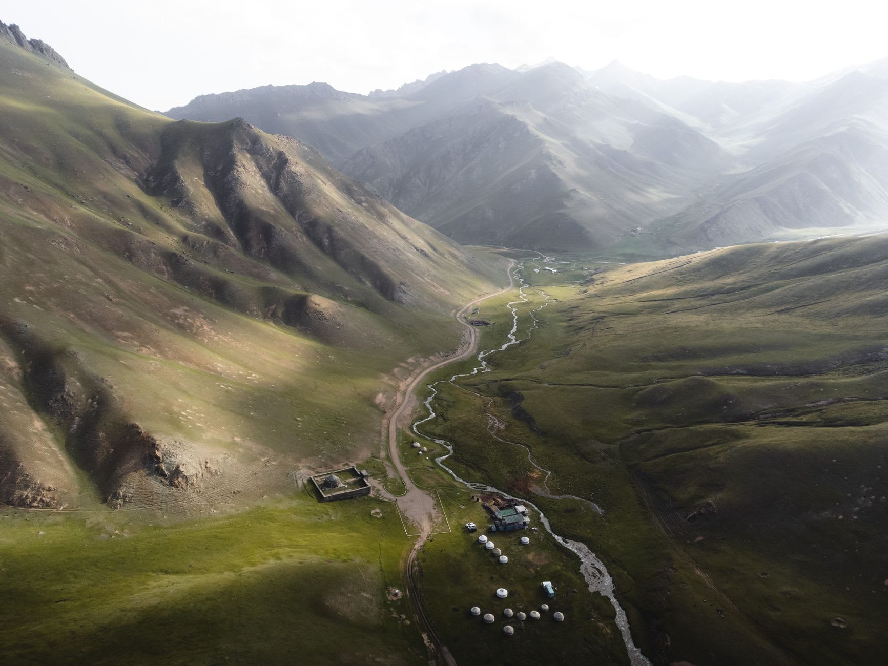 Horses grazing on the green alpine meadows of Altyn-Arashan with a herder's yurt and the snow-streaked peaks of the Terskey Ala-Too in the distance