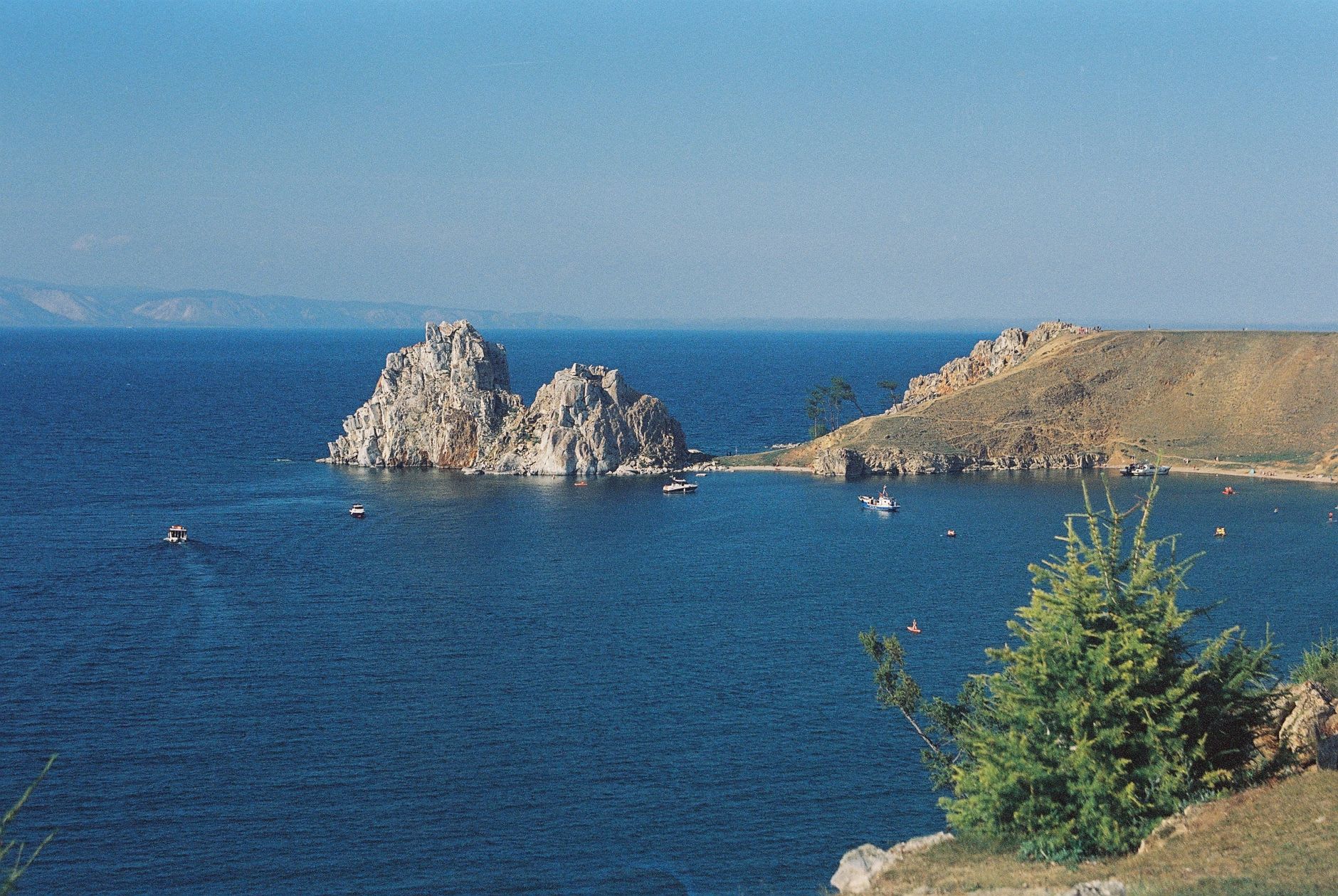 The stone entrance of a Circum-Baikal tunnel cut through solid cliff, the lake visible just beyond in brilliant afternoon light