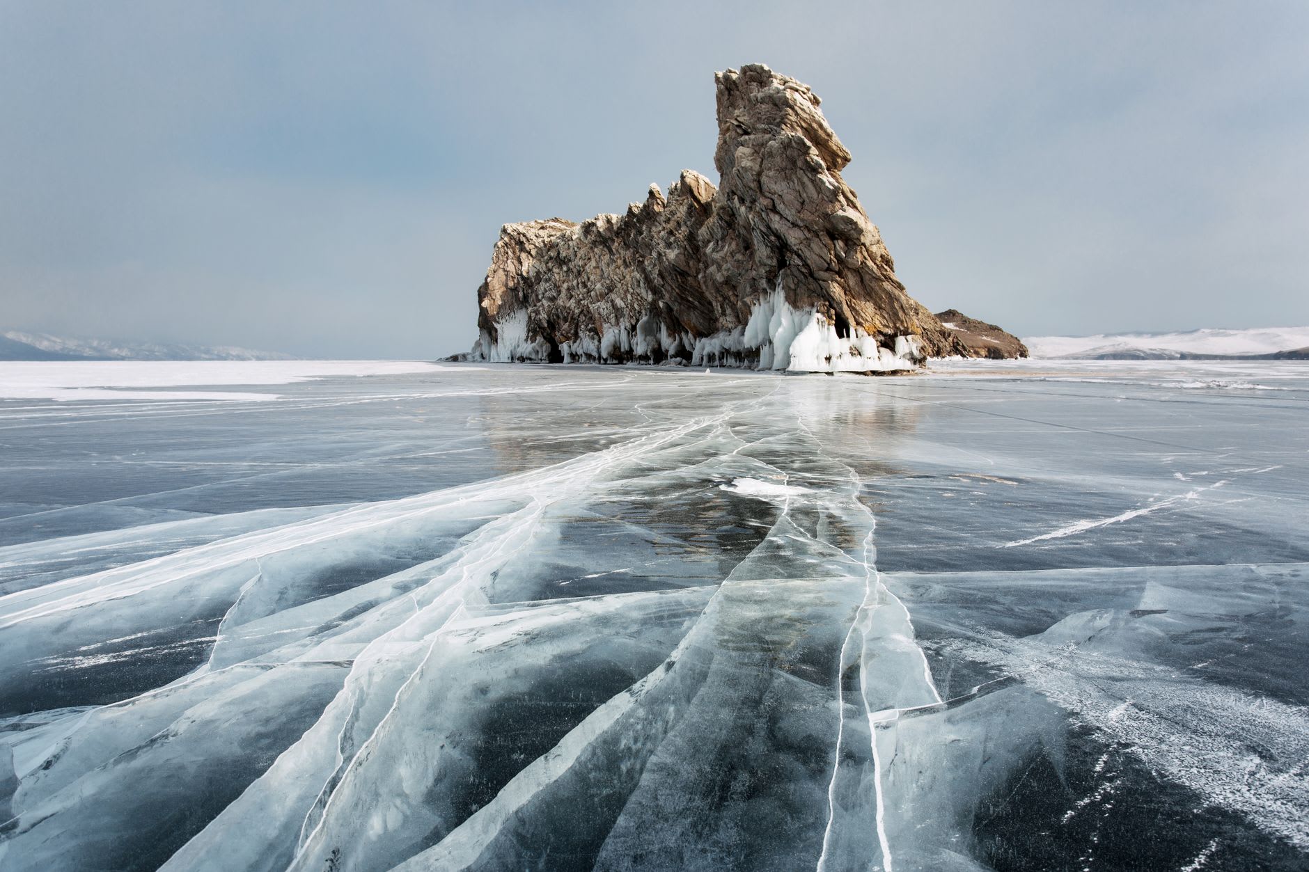 Burkhan Rock at sunrise, its twin marble pillars catching the pink light over the unmarked ice of Khuzhir Bay