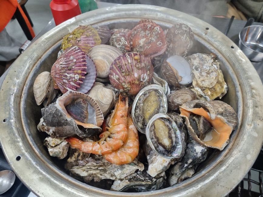 Un tradicional pozo de curanto siendo destapado en Isla Tenglo, con vapor elevándose de mariscos, papas y milcao