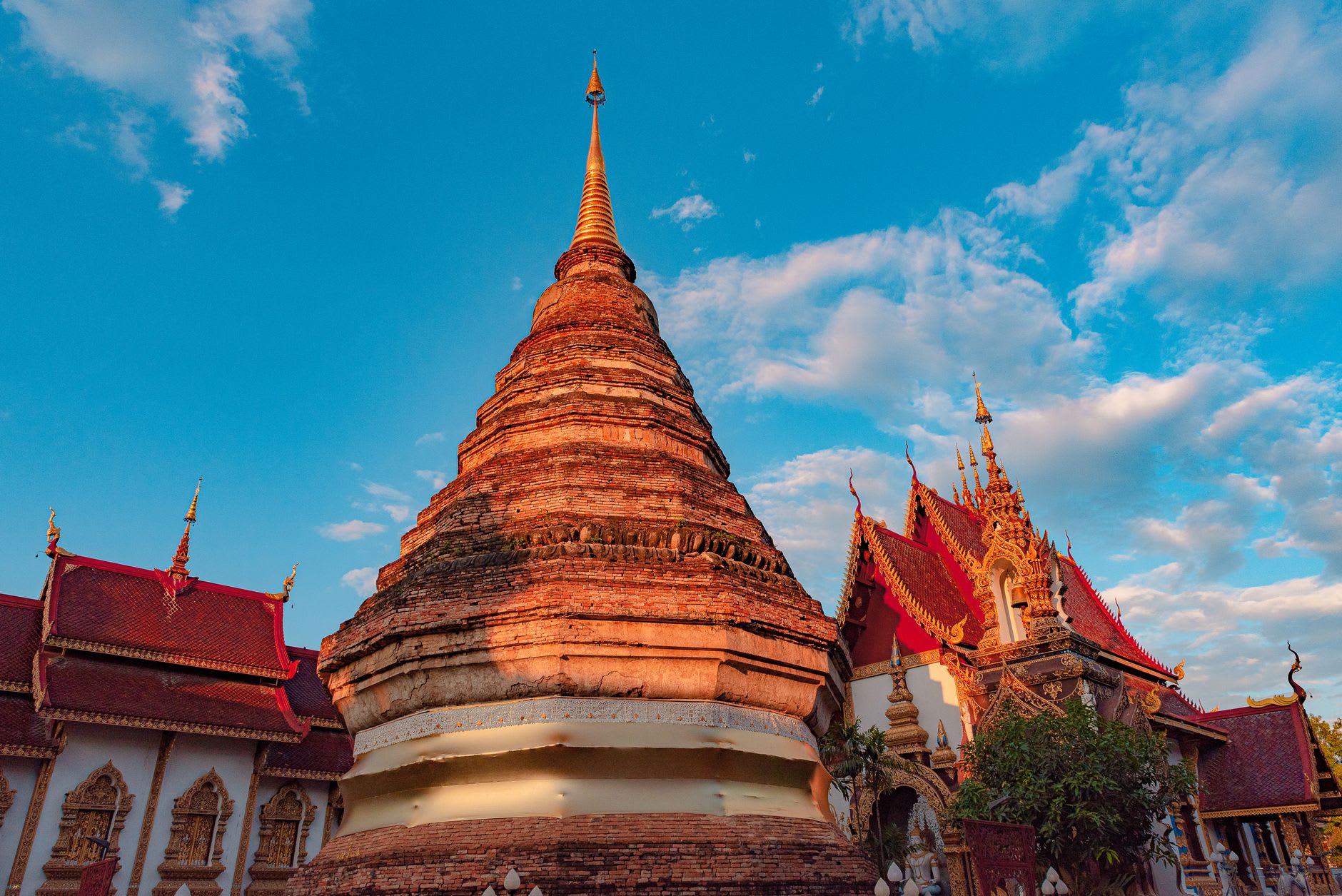 That Luang stupa glowing deep gold in the late afternoon sun, smaller chedis surrounding the central tower, orange-robed monks in the foreground