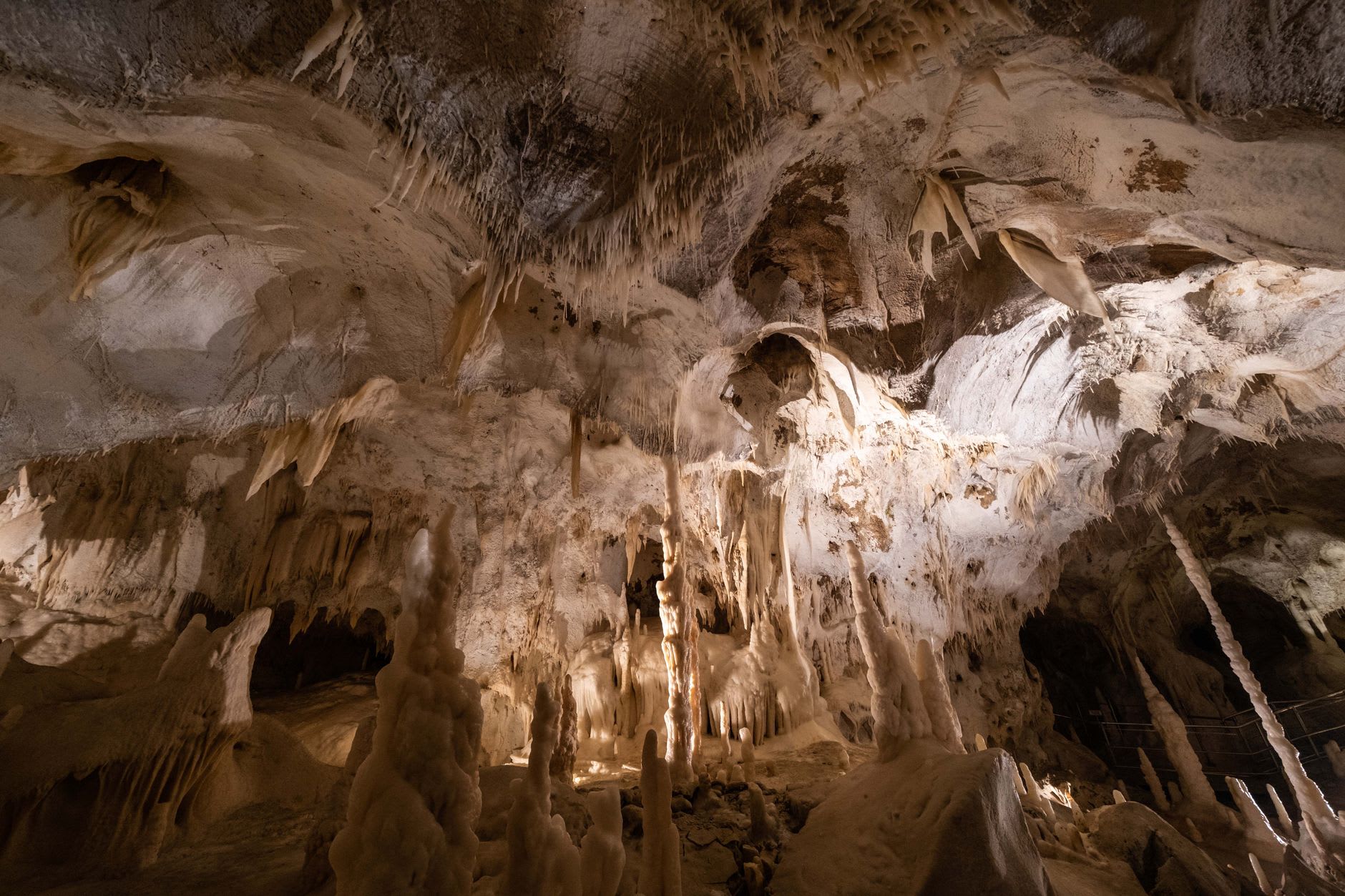 Vast stalactite and stalagmite formations in Jeita Grotto's upper cavern, their scale dwarfing the raised wooden walkway threading between them