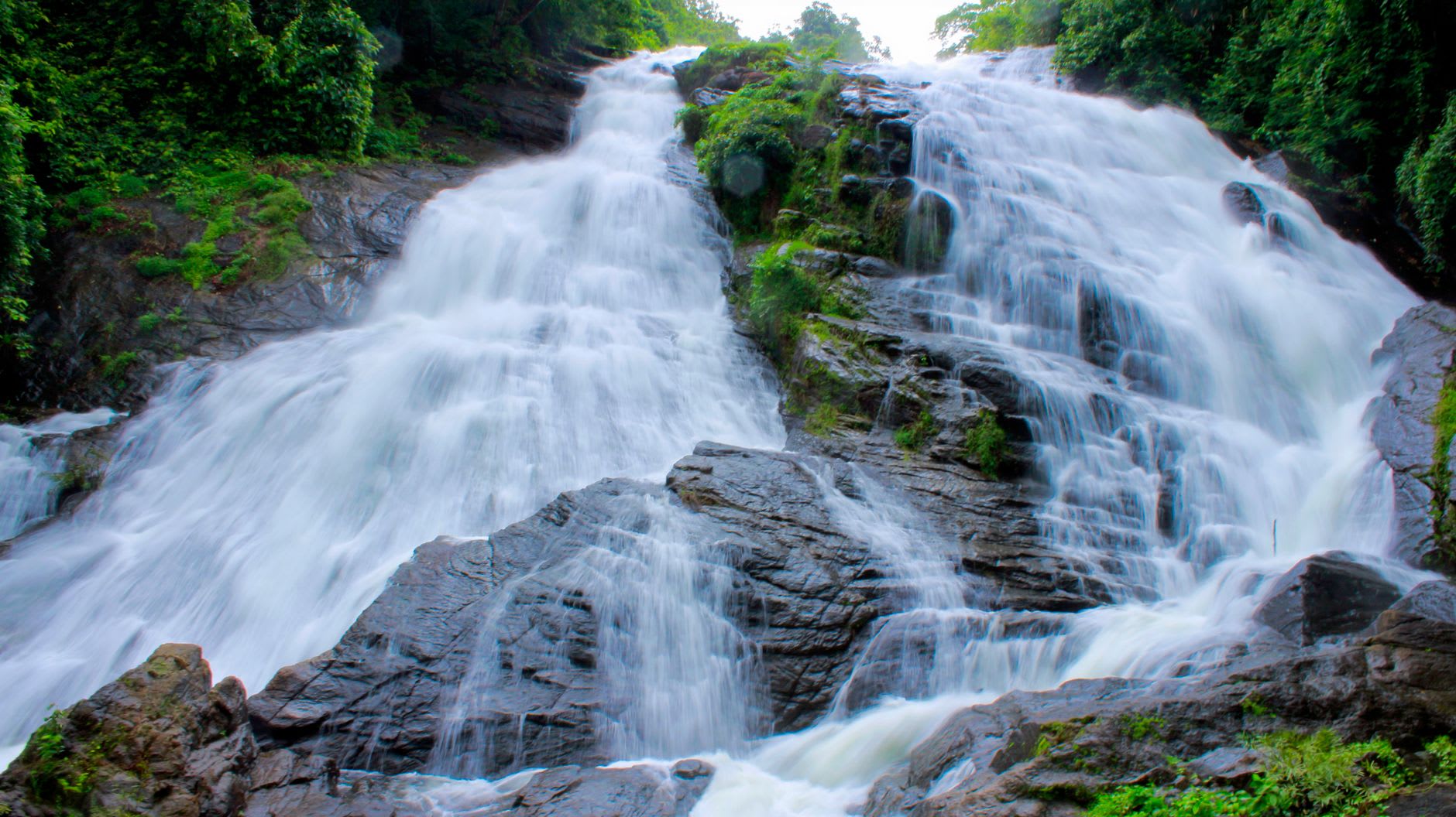 The upper tier of Kpatawee Falls seen from below, water white against dark rock, forest closing in on all sides