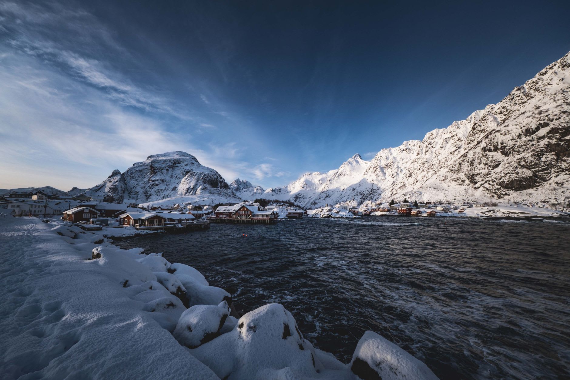Hamnøy bridge at first light in February, red rorbu reflecting perfectly in still water, mountains in cloud above