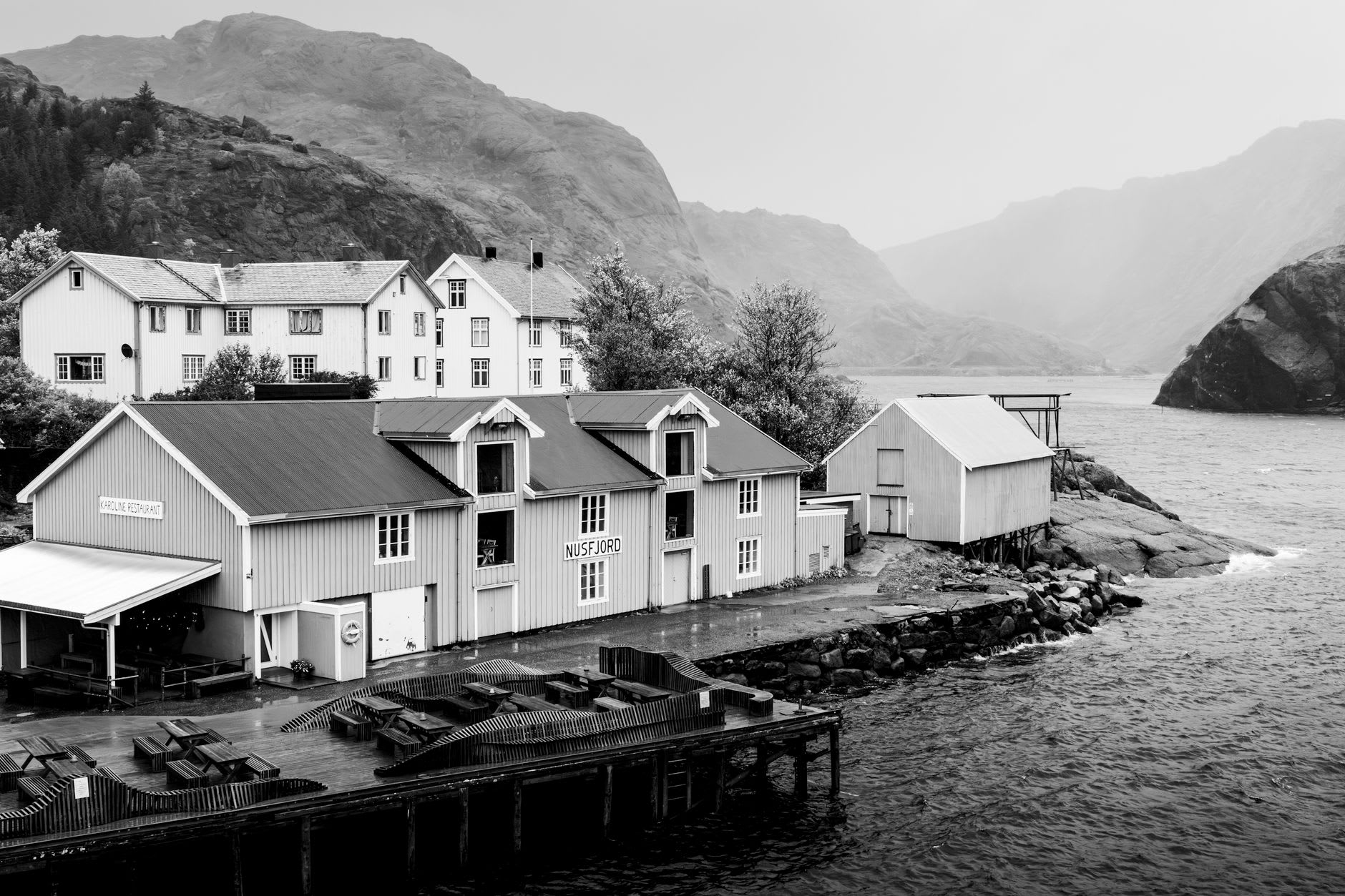 Nusfjord general store exterior, unchanged facade from 1878, dried fish hanging in the doorway, fog on the mountain above