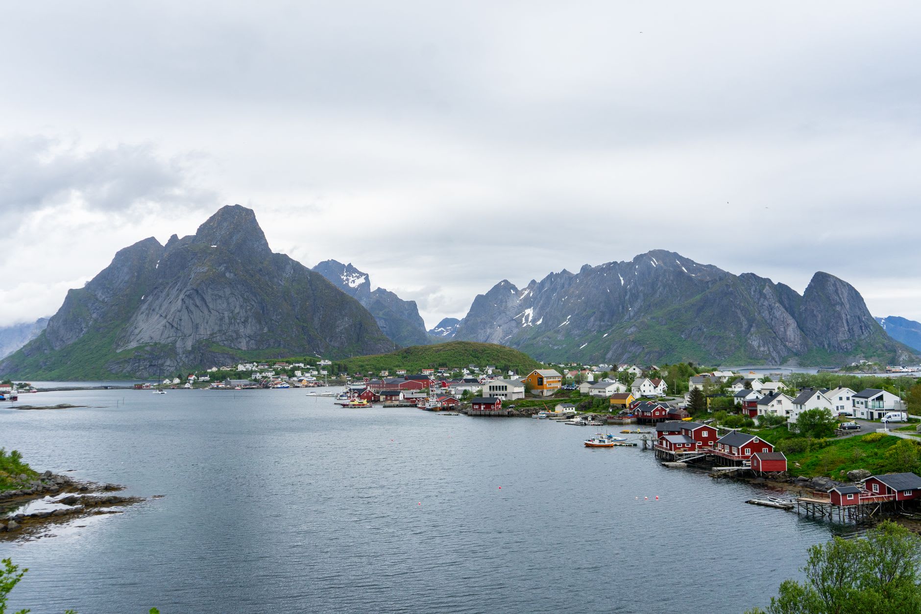 Red rorbu fishing huts glowing at dusk beside Reine's fjord, snow-streaked mountains rising behind