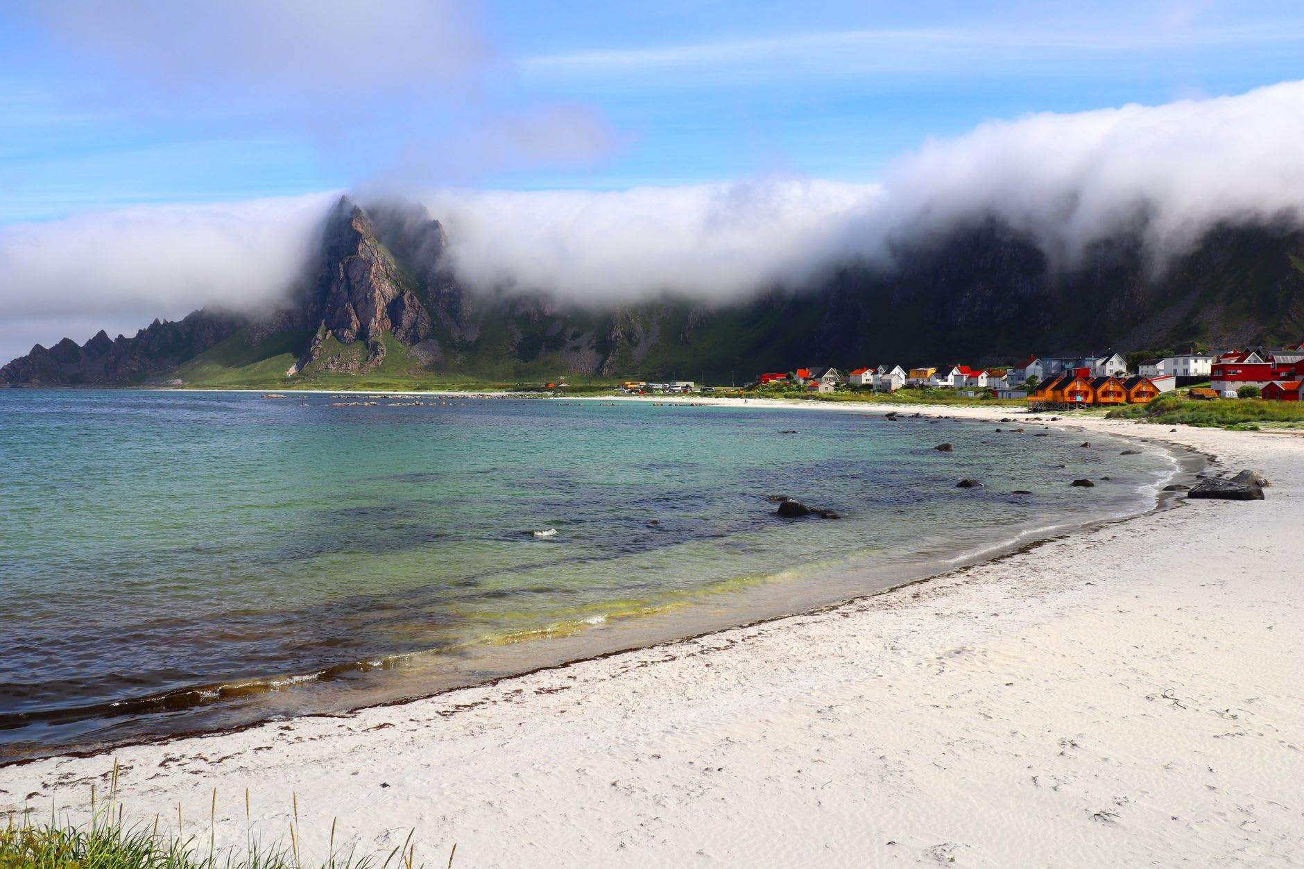 Unstad valley from above: the beach at the foot of steep mountains, a set of waves breaking, surfers small in the water