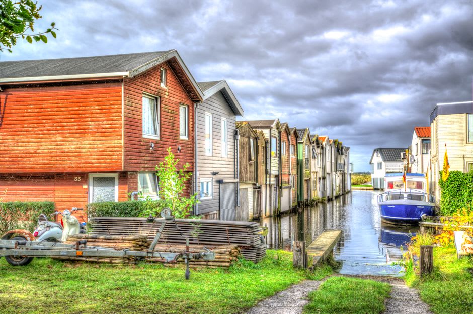 Una casa sobre pilotes construida directamente sobre el agua quieta del Canal de Pangalanes, rodeada de palmas de rafia al atardecer