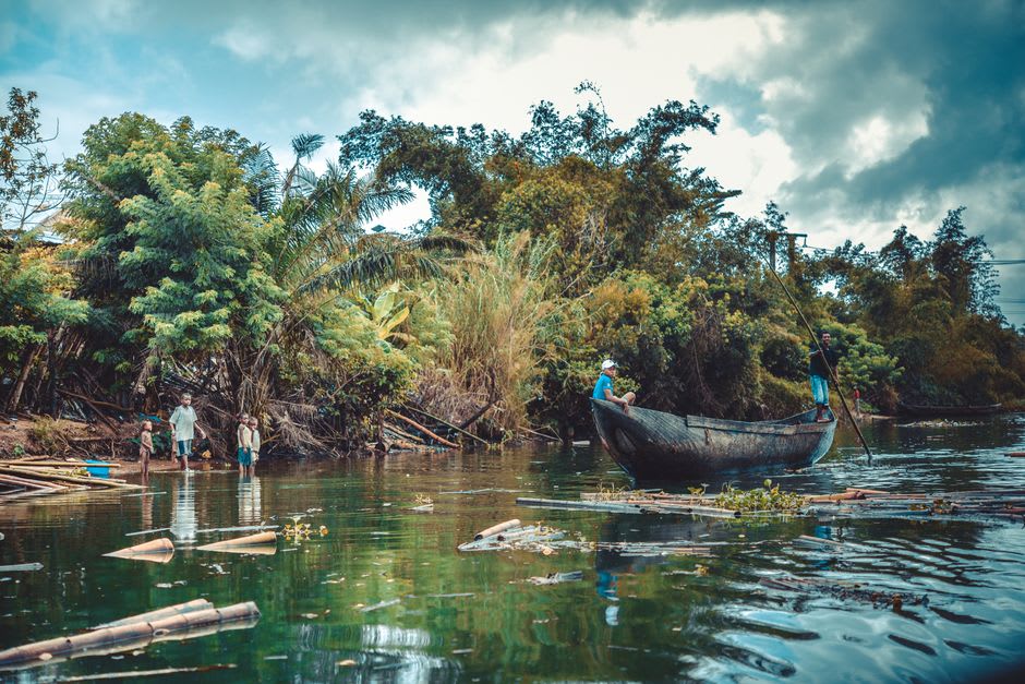 Una canoa de madera deslizándose en silencio por un tramo quieto y bordeado de palmeras del Canal de Pangalanes al final de la tarde