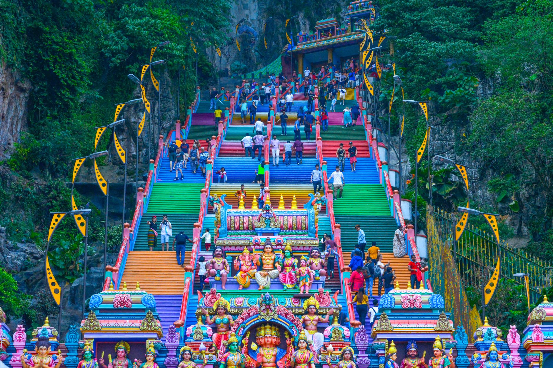 Shafts of daylight falling into the vast Temple Cave at Batu Caves, illuminating a Hindu shrine set into the limestone