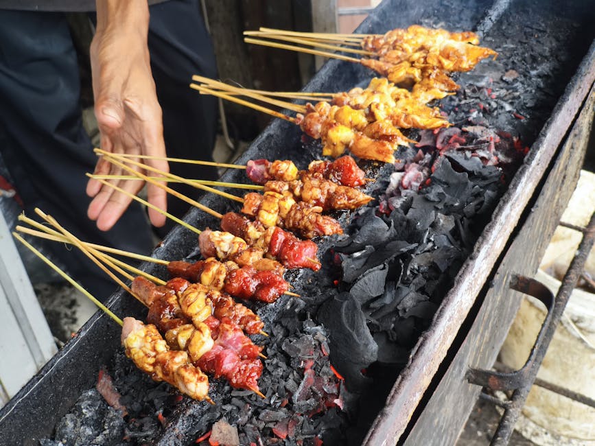 Skewers of satay celup being dipped in bubbling peanut sauce
