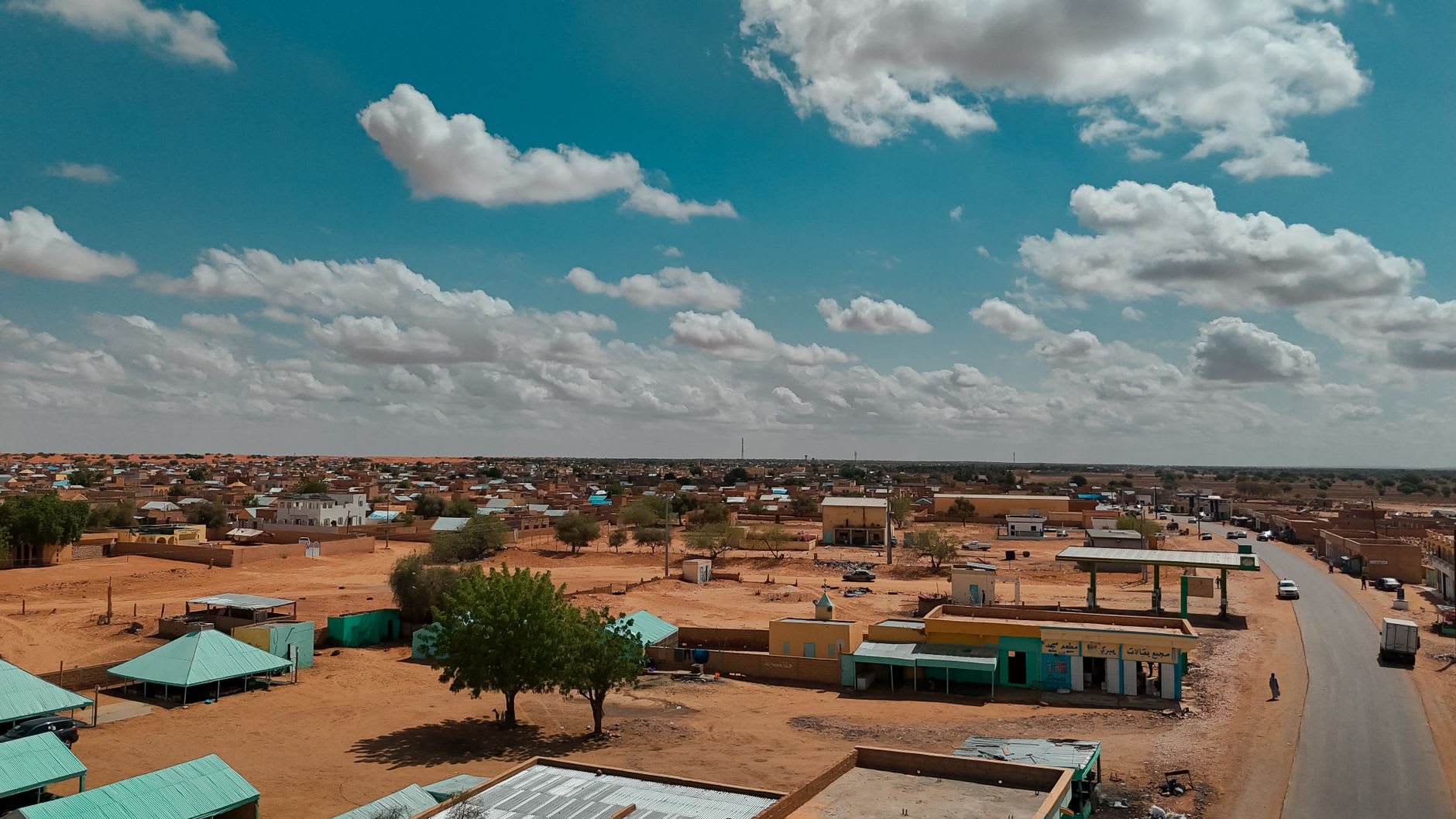 Un taller de bogolan en Ségou, tiras de algodón secándose en una cuerda tendida entre árboles, sus patrones geométricos negros y ocre visibles bajo la luz de la tarde
