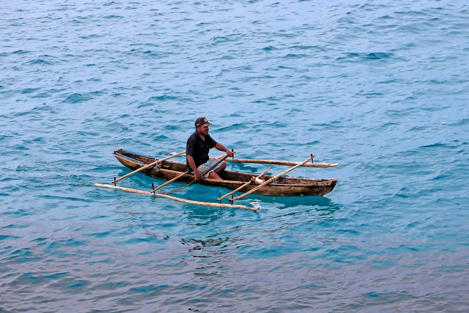 A Marshallese canoe builder shaping the hull of a wooden outrigger canoe on the sand at Likiep