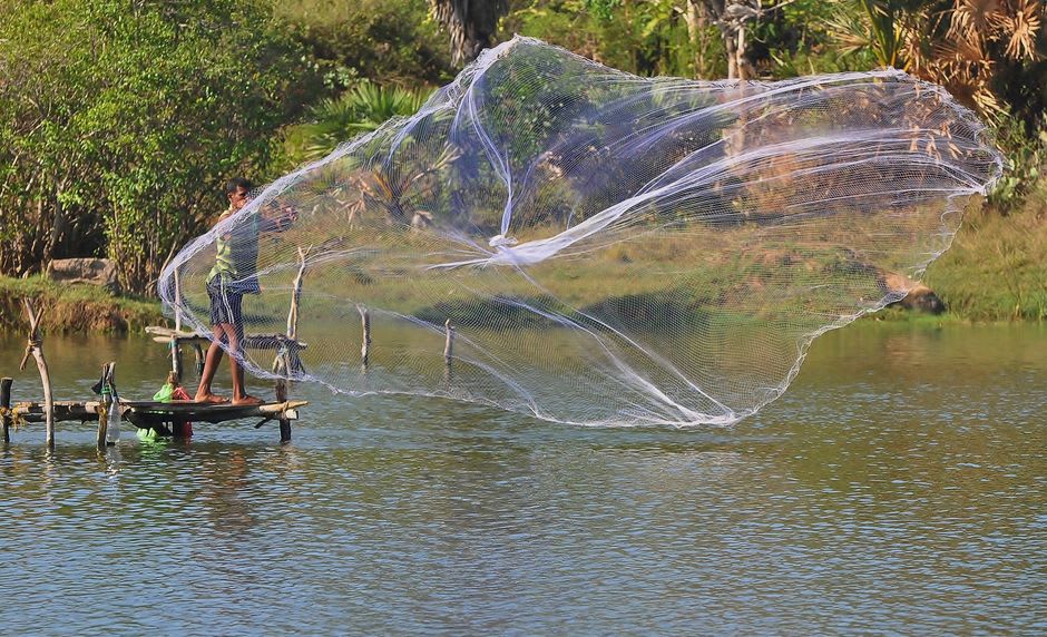 Local children fishing with handlines from a wooden dock on Namdrik's calm lagoon in late afternoon light