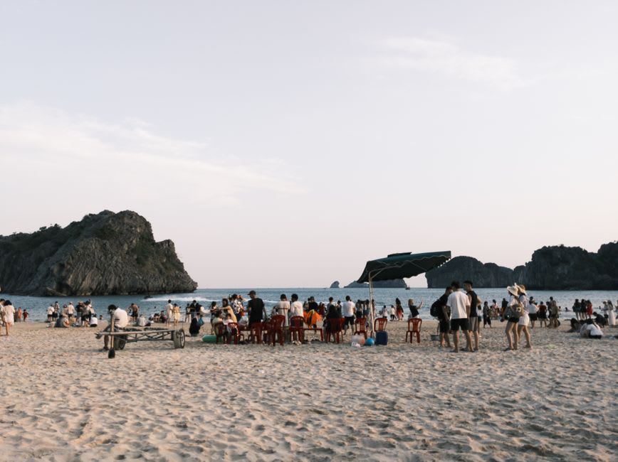 Des familles rassemblées sur la plage au coucher du soleil devant les maisons de l'îlot principal de Namu