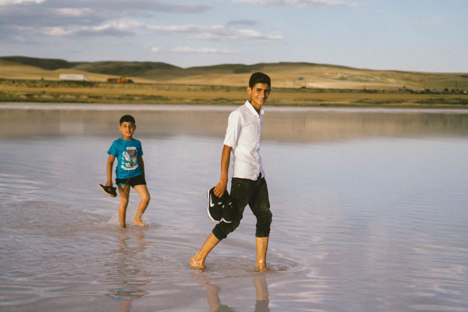 Two teenage boys wading in the shallow turquoise lagoon of Ujae carrying a homemade spear and a catch of reef fish